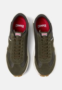 Grüne Sneakers aus einer Mischung von Leder und Wildleder. Sie verfügen über Schnürsenkel, ein gepolstertes rotes Innenfutter und eine weiße Sohle mit braunen Akzenten.