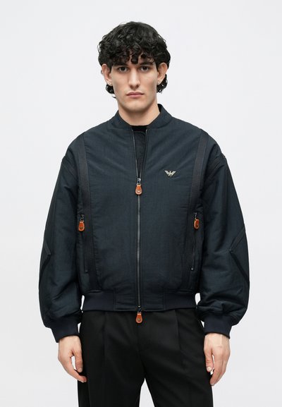 Čierna bomber bunda z textúrovanej látky so zipsom na prednom diely, rebrovanými manžetami a hnedými jazdcami na zips; na hrudi malý logo.