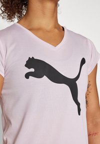 Camiseta de cuello en V rosa, hecha de una tela suave, con un gran logo negro de Puma en posición de salto en la parte frontal. Mangas cortas.