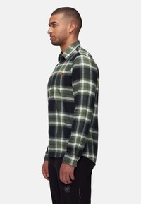 Camicia a maniche lunghe a quadri in verde, nero e bianco. Presenta chiusura con bottoni, colletto e taschino sul petto con logo. Tessuto di texture morbida.