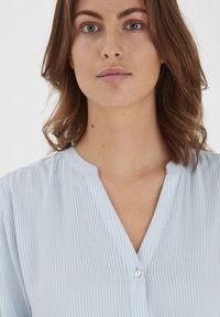 Light blue striped shirt with a v-neck and button detail. The fabric appears smooth and lightweight, featuring thin vertical stripes.