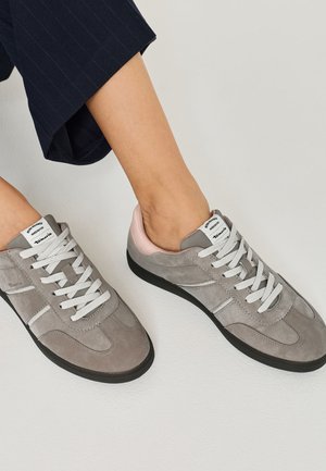 Szare zamszowe sneakersy z białymi sznurówkami i czarnymi podeszwami. Udekorowane jasnoróżowym akcentem przy pięcie, z klasycznym sportowym wzornictwem.