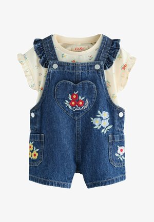 Baby romper i denim med blomsterbroderi på lommer og hjertepatch på brystet, lagt over en cremefarvet skjorte med små blomsterprint og flæseærmer.