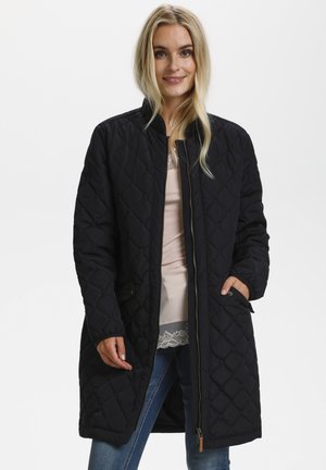 Veste noire matelassée avec fermeture éclair, col côtelé et poches latérales ; présente une texture lisse et un motif en diamant sur l'ensemble.