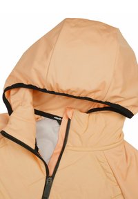 Chaqueta de color durazno con capucha forrada, cremallera frontal y ribete negro. Presenta costuras diagonales y un exterior suave y texturizado.