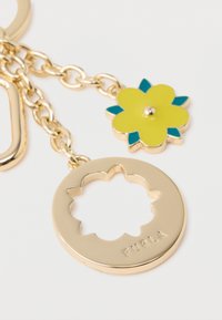 Arany színű fém kulcstartó kerek medállal, virágos kivágásos mintával, sárga és türkiz színű virágos akcentussal.