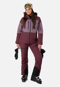 Ski-jakke og -bukser i maroon og lavendel, med lynlåse, hætte og handsker. Tekstureret, vandtæt materiale til vintersport.