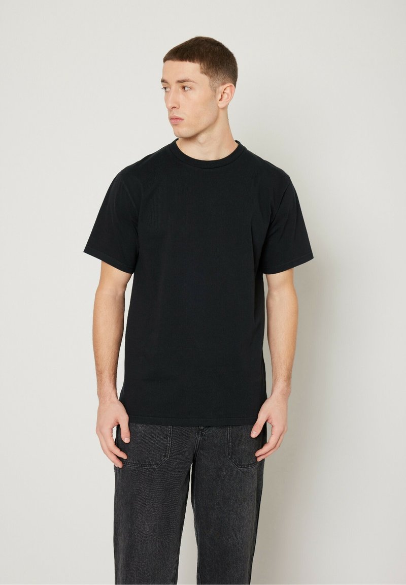 Maglietta nera in cotone a maniche corte con scollatura rotonda, abbinata a jeans grigio scuro. Il tessuto è morbido e presenta un design semplice.