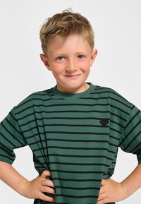 Grön randig t-shirt med svarta horisontella ränder, rund halsringning och en liten svart broderad logga på vänster sida.