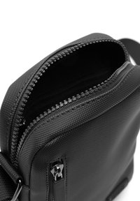 Borsa a tracolla nera texturizzata con chiusura a zip, dotata di un binario per zip fluido e una piccola tasca esterna. Forma rettangolare compatta.