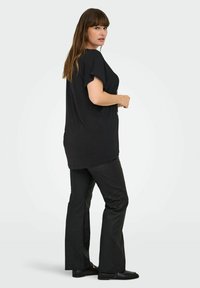 Crna majica s kratkim rukavima u kombinaciji s crnim zvonastim hlačama. Majica ima labav kroj i mekanu teksturu. Upadljivi detalji uključuju jednostavan dizajn i minimalne akcentne.