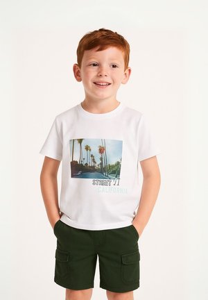 Vit t-shirt med en palmträdsgrafik och texten "STREET 11 CALIFORNIA", tillsammans med gröna cargoshorts. Barnet visar ett neutralt uttryck.