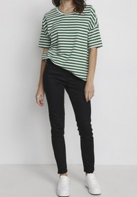 Camiseta de manga corta a rayas verdes y blancas combinada con jeans skinny negros y zapatillas blancas. La tela parece suave y tiene un corte relajado.