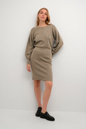 Beige knitted sweater with a round neckline and long sleeves, paired with a fitted beige skirt. Model wears shiny black platform shoes.