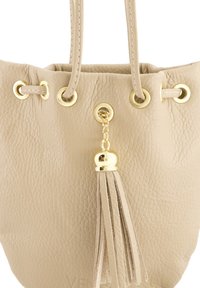 Beige leren emmer tas met gouden hardware en eyelets. Voorzien van een hangende franjes accent en een gestructureerde oppervlakte. Open bovenkant ontwerp.