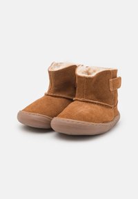 Botas de tobillo de ante marrón con un suave forro de pelo y una correa de Velcro. Punta redonda y suela de goma para mayor tracción. Diseño sencillo y textura cálida.