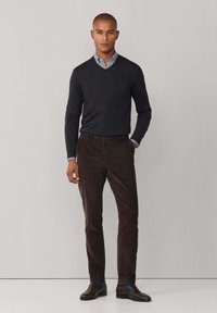 Donkergrijze v-halstrui over een lichtblauw geruit shirt, gecombineerd met donkerbruine broek en bruine leren schoenen, wat zorgt voor een gelaagde uitstraling.