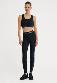 Svart sport-bh och högmidjade leggings som är gjorda av ett slätt tyg. Leggings har ett tonalt geometriskt mönster och en märkesmidja. Matchande svarta sneakers.
