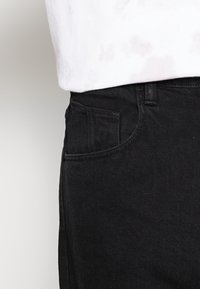 Czarne dżinsy z klasycznym prostym krojem, z boczną kieszenią i teksturowanym materiałem. Nosi się je z jasnym t-shirtem.