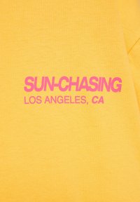 Tissu jaune avec texte rose indiquant « SUN-CHASING LOS ANGELES, CA » en styles de police gras et normal.