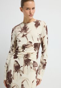 Długo rękawowy top z kwiatowym wzorem w odcieniach brązu i beżu. Posiada dopasowany krój z marszczeniami oraz okrągłym dekoltem.