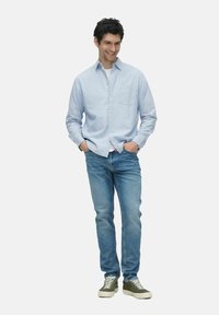 Chemise bleu clair à boutons, jean en denim et baskets vertes. La chemise a une poche sur la poitrine ; le jean est de coupe standard ; textures lisses.