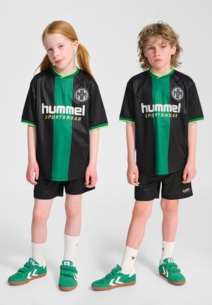 To børn, der står side om side iført sorte og grønne Hummel sportstøjstrøjer, shorts, hvide sokker og grønne sneakers.