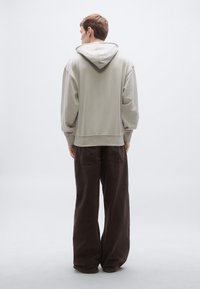 Helehall kapuutsiga pusa lõdva lõikega, soonikkoes mansettide ja nööriga kapuutsiga, kombineeritud tumepruunide laiade pükstega. Sile tekstuur, minimalistlik disain.