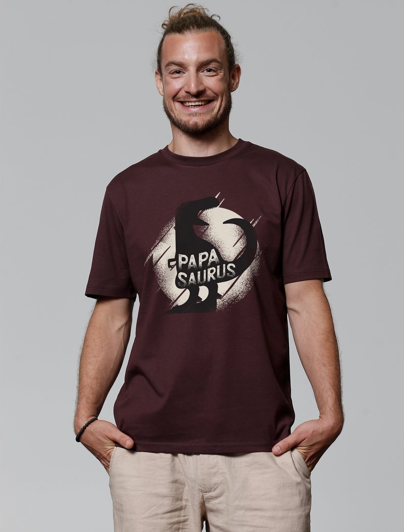 Bordeauxrotes T-Shirt aus einer Baumwollmischung, mit einem auffälligen schwarzen Dinosauriergrafik und dem Text "Papa Saurus" in Weiß auf einem strukturierten Hintergrund.