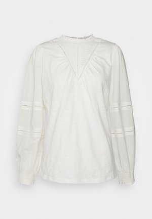 Blusa blanca de manga larga con detalles de encaje en el pecho y las mangas, cuello alto fruncido y puños, corte holgado.