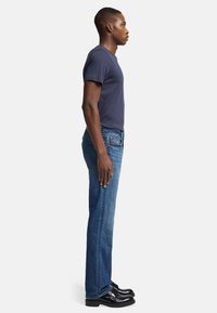 Granatowa koszulka zestawiona ze spodniami dżinsowymi w średnim odcieniu, o prostym kroju i delikatnym wyblaknięciu, uzupełniona czarnymi butami na sznurówki.