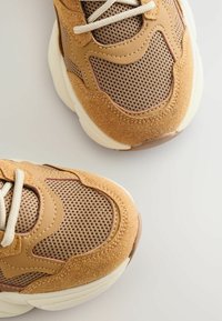 Brązowe sneakersy z siateczkowymi wstawkami i zamszowymi akcentami. Posiadają chunky podeszwę i miękkie beżowe sznurowadła. Teksturowana cholewka, zaokrąglony czubek.