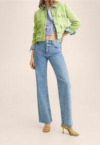 Grøn tweed cropped jakke med guldknapper, blå og hvid stribet skjorte, højttaljede lyseblå jeans og grønne strophæle.
