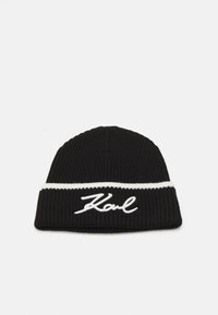 Bonnet en tricot noir avec une bande blanche et un logo "Karl" brodé en cursive. La texture est côtelée pour plus de chaleur et de style.