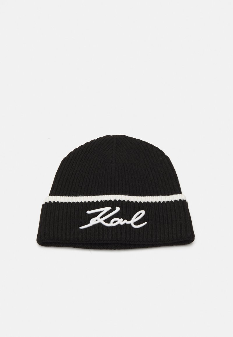 Bonnet en tricot noir avec une bande blanche et un logo "Karl" brodé en cursive. La texture est côtelée pour plus de chaleur et de style.