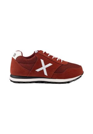 Zapatilla deportiva roja con cordones blancos, logo blanco "X" en el lateral, suela negra y blanca, y lengüeta blanca en el talón con el nombre de la marca.