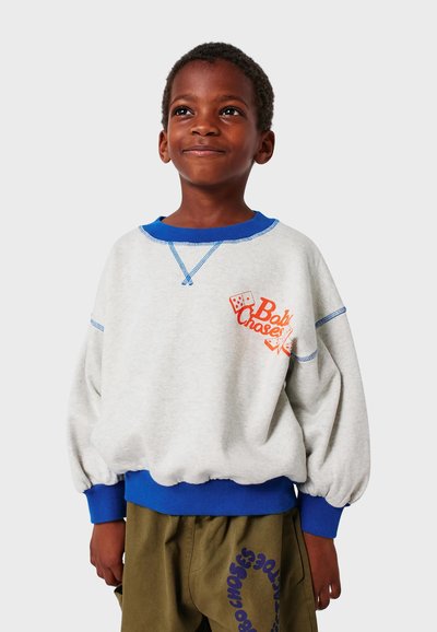 Sivi dukserica s plavim naglascima, s округлим izrezom i napuhanim rukavima. Na prsima ima narančasti tekst i grafiku kockica.