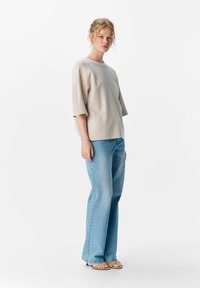Lys beige kortærmet sweater med blød tekstur parret med lyseblå flared jeans og sorte sandaletter med stropper. Enkel, afslappet påklædning.
