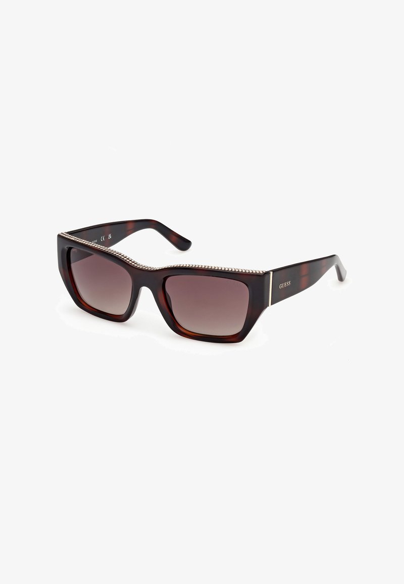 Lunettes de soleil rectangulaires en écaille de tortue avec des verres dégradés marron, des accents en strass sur la monture supérieure et un logo "GUESS" sur la branche.
