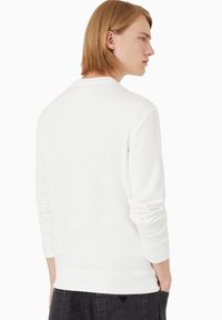 Felpa bianca con maniche lunghe, collo tondo e polsini a coste. Texture liscia con un design minimalista e senza motivi o loghi visibili.