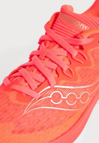 Φωτεινό κοραλί ροζ παπούτσι τρεξίματος Saucony με επίπεδα κορδόνια και λευκό λογότυπο σε υφασμένο διχτυωτό επάνω μέρος.