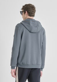 Felpa grigia con cappuccio e coulisse, vista posteriore, maniche a coste e fondo a coste, realizzata in un materiale morbido e liscio.