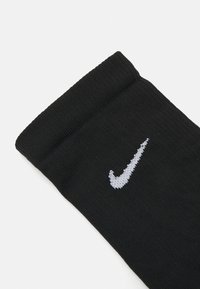 Melna kokvilnas zeķe ar teksturētu ribu dizainu, uz kuras augšdaļas ir izšūts balts Nike swoosh logo.