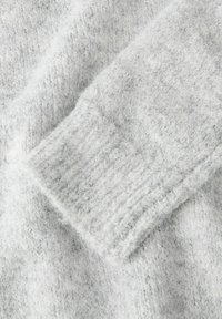 Manche de pull en tricot gris clair doux avec détail de bord-côte, montrant une texture duveteuse et des fibres de laine étroitement tissées.