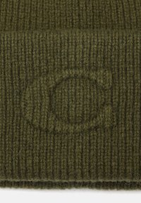 Gorro de punto verde oliva con textura acanalada, con un sutil logo circular en relieve en la tela. Material suave similar a lana.