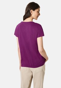 T-shirt corto viola a maniche corte con scollatura rotonda e vestibilità rilassata. Tessuto testurizzato e design semplice, abbinato a pantaloni di colore chiaro.