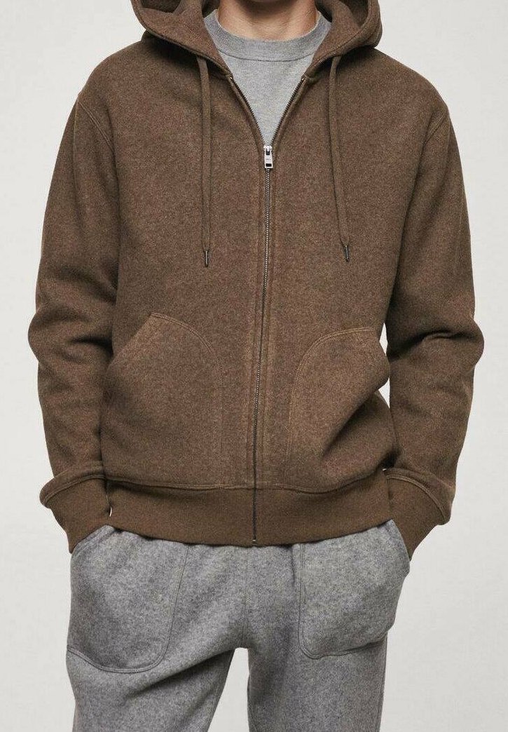 Sweat à capuche marron à fermeture éclair avec poches avant, capuche avec cordon et poignets côtelés. Associé à un pantalon de survêtement gris avec poches latérales.