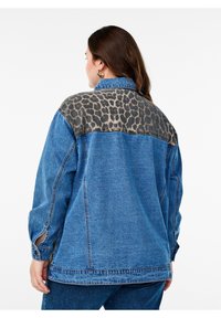 Džínová bunda s leopardím potiskem na ramenech. Má uvolněný střih, dlouhé rukávy a zapínání na knoflíky na manžetách. Převážně modrá s akcenty zvířecího vzoru.