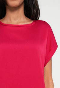 Fuchsiové tričko s krátkými rukávy a kulatým výstřihem, vyrobené z hladké tkaniny. Má volný střih a minimální švy.