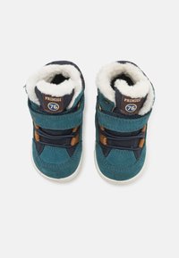 Bottes montantes en daim bleu et marine avec doublure en fausse fourrure beige, dotées de deux sangles réglables et d'une semelle ronde en caoutchouc blanc.